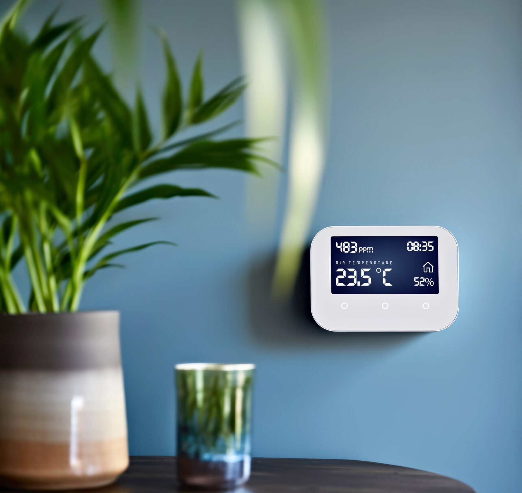A touchscreen thermostat with air quality and temperature control system installed on a blue home wall. Smart home technology enhancing daily comfort and domestic living