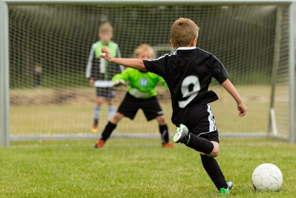 A young boy in a black soccer jersey with the number 9 prepares to kick a soccer ball toward a goal